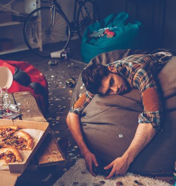 Person liegt über einem Schlafsack in einem unaufgeräumten Zimmer