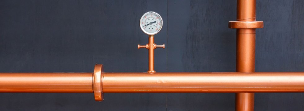 Bronzefarbig Rohre mit einem Messgerät auf dunkelgrauer Wand
