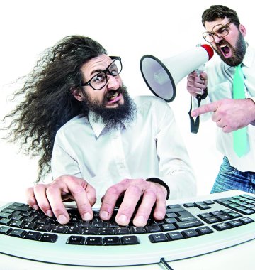 Zwei Arbeiter vor dem Computer von denen der eine vom anderen mit dem Megaphon angeschriehen wird