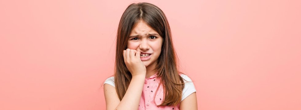 Mädchen vor pfirsichfarbenen Hintergrund kaut auf ihren Fingernägeln