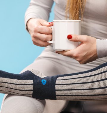 sitzende Frau mit einer Tasse und ihrem Fuß auf dem anderen Bein abgestützt